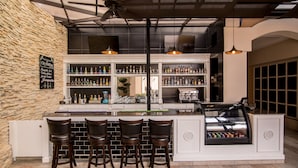 A bar area with a stone wall, a counter with stools, and shelves stocked with bottles. - Hilton Princess Managua (Managua)