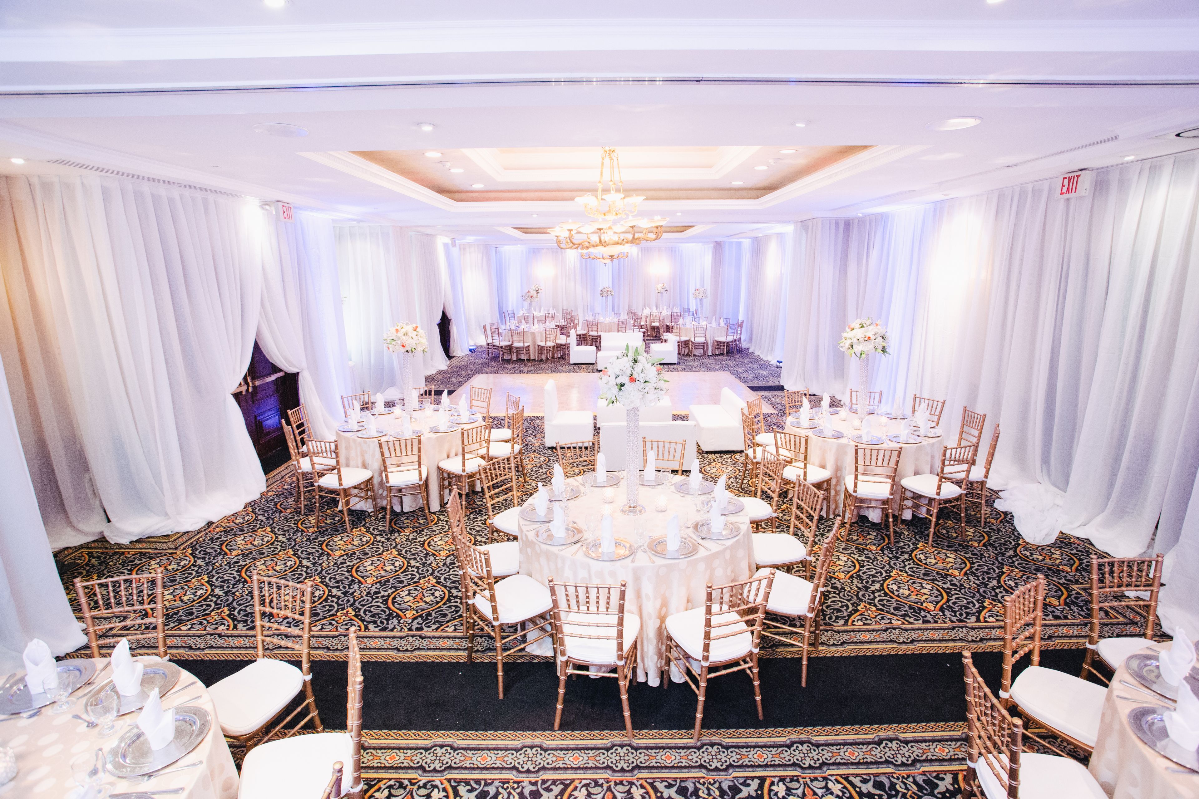 A banquet hall with round tables, white drapes, and a patterned carpet.