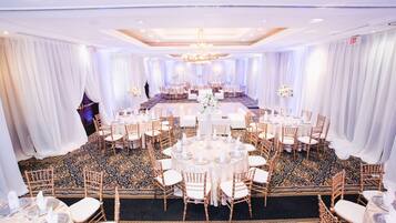 A banquet hall with round tables, white drapes, and a patterned carpet.