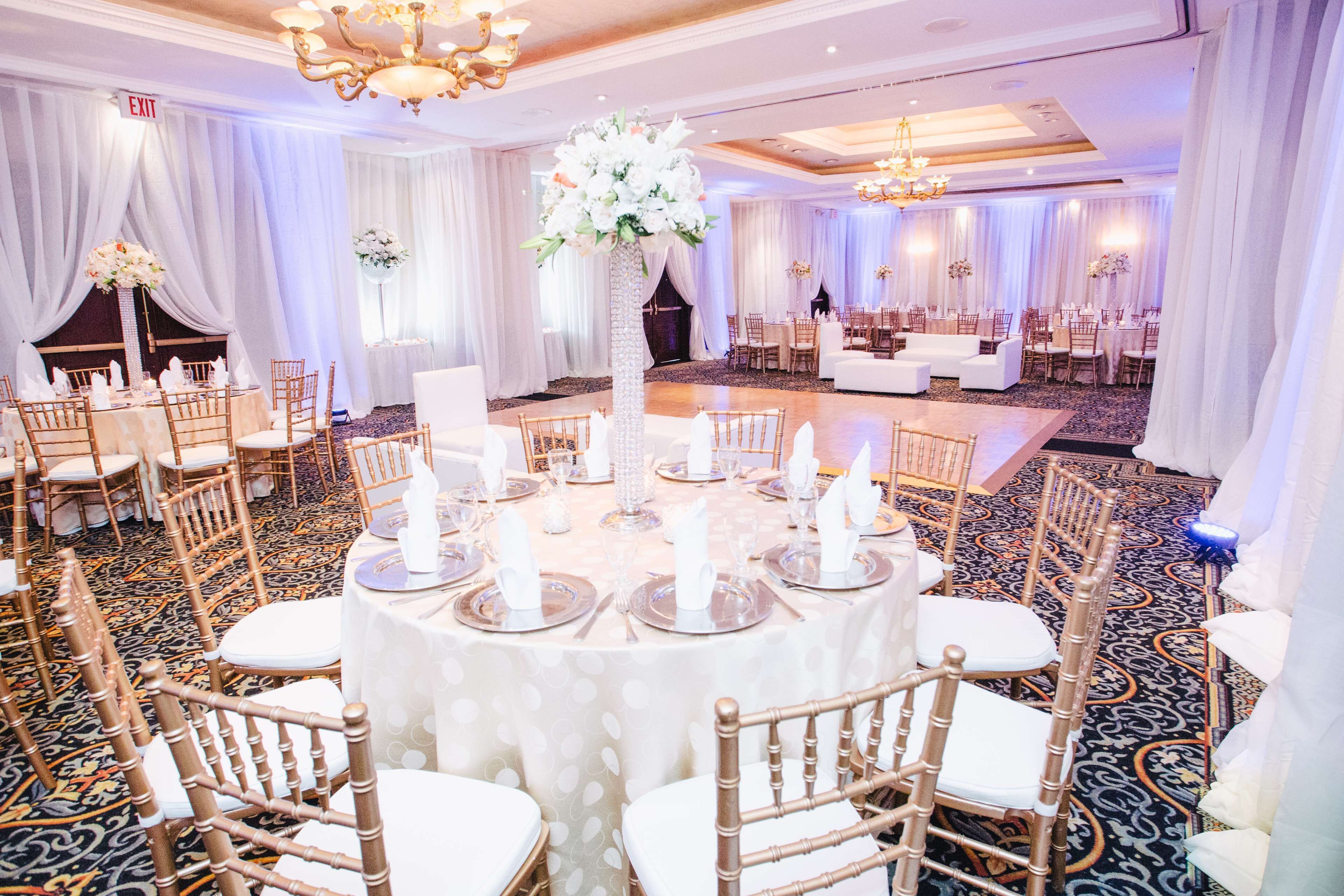 A banquet hall with round tables, white tablecloths, and gold chairs.
