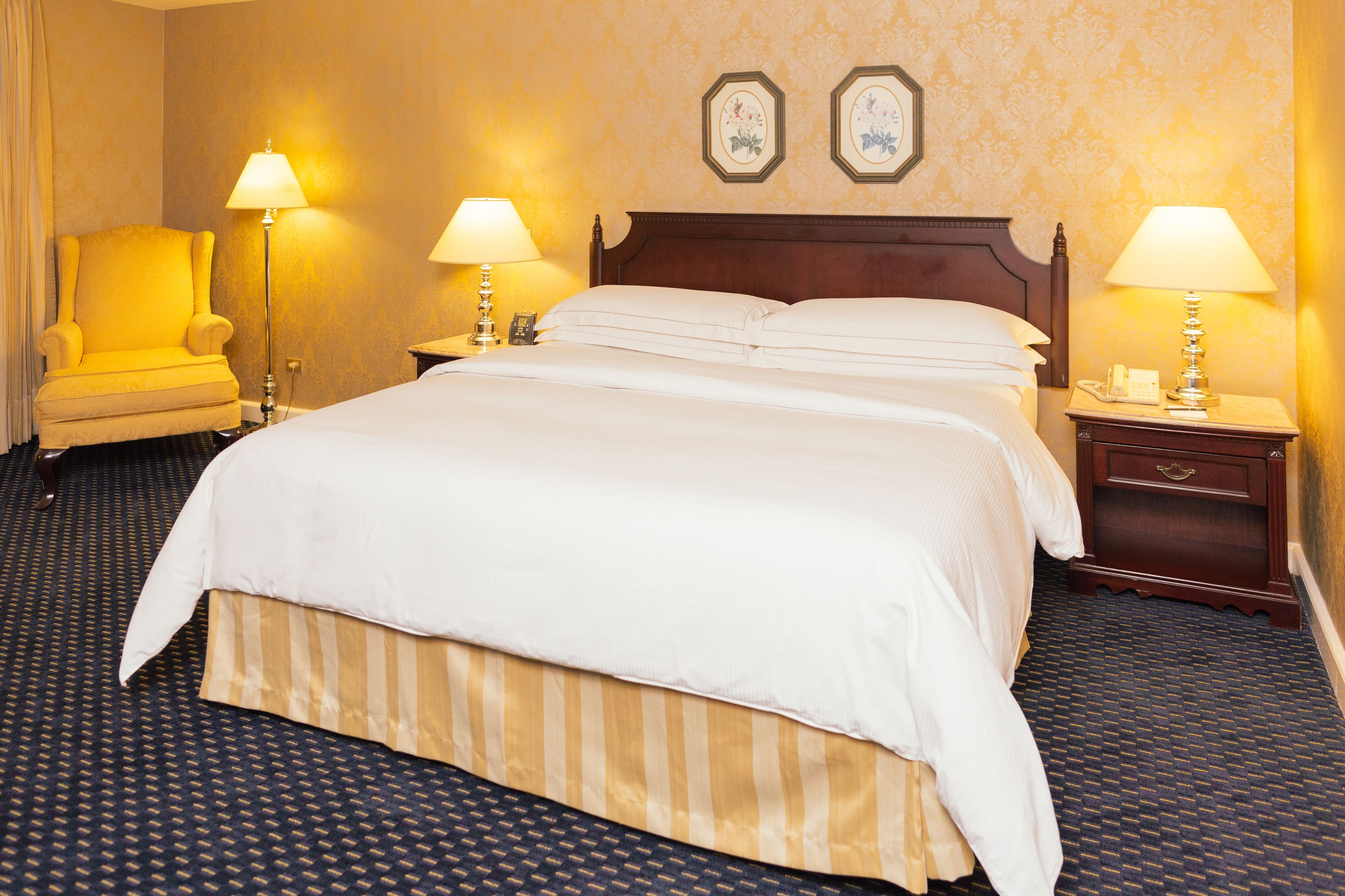 Ein Hotelzimmer mit einem großen Bett, zwei Nachttischen mit Lampen, einem Sessel und Teppichboden.
