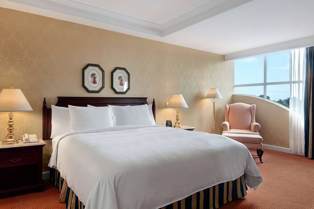 A hotel room with a large bed, two bedside tables with lamps, a chair, and a view of the outdoors.