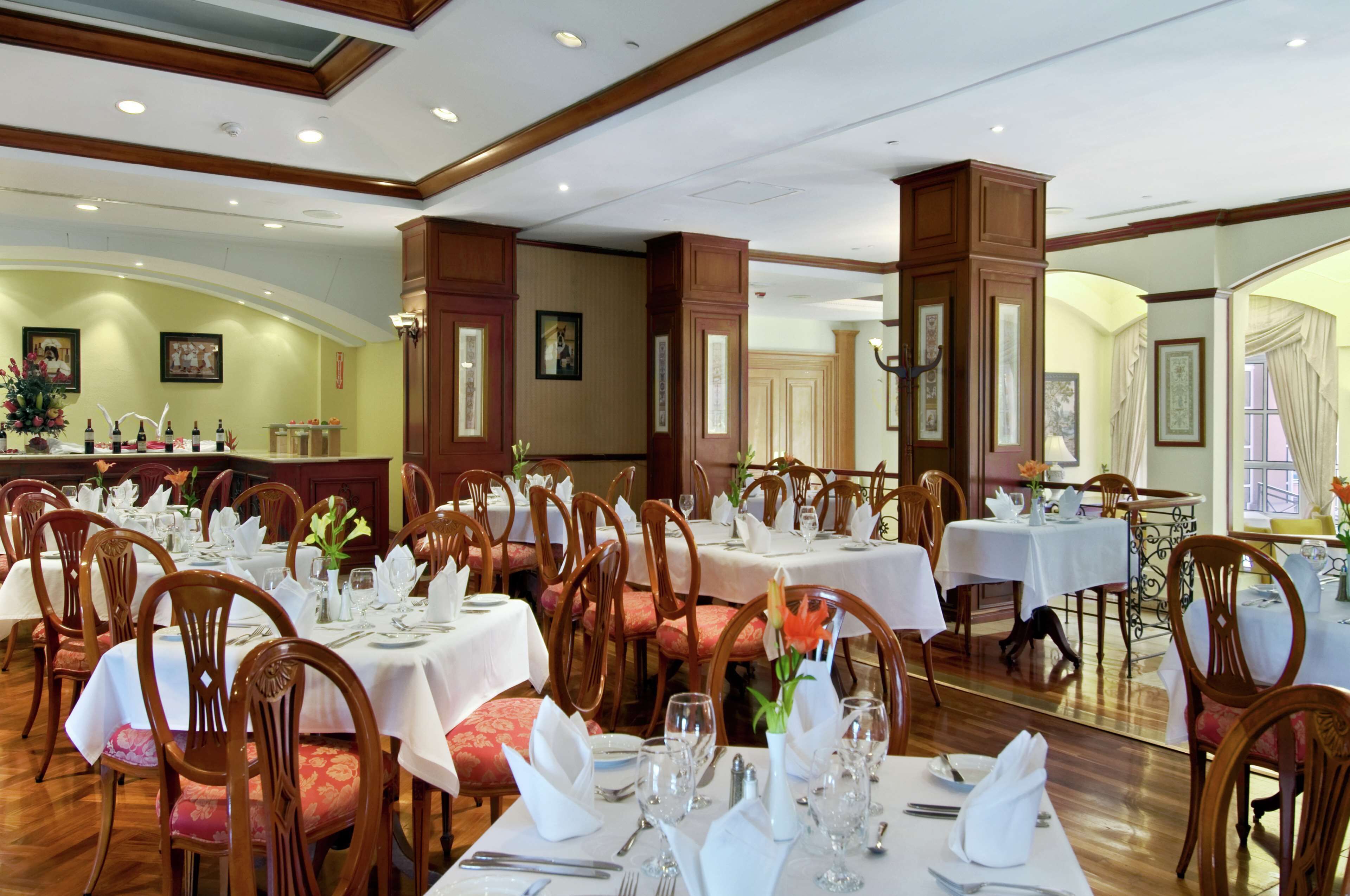 A formal dining room with multiple tables set for service, wooden chairs, and a large mirror reflecting the room.