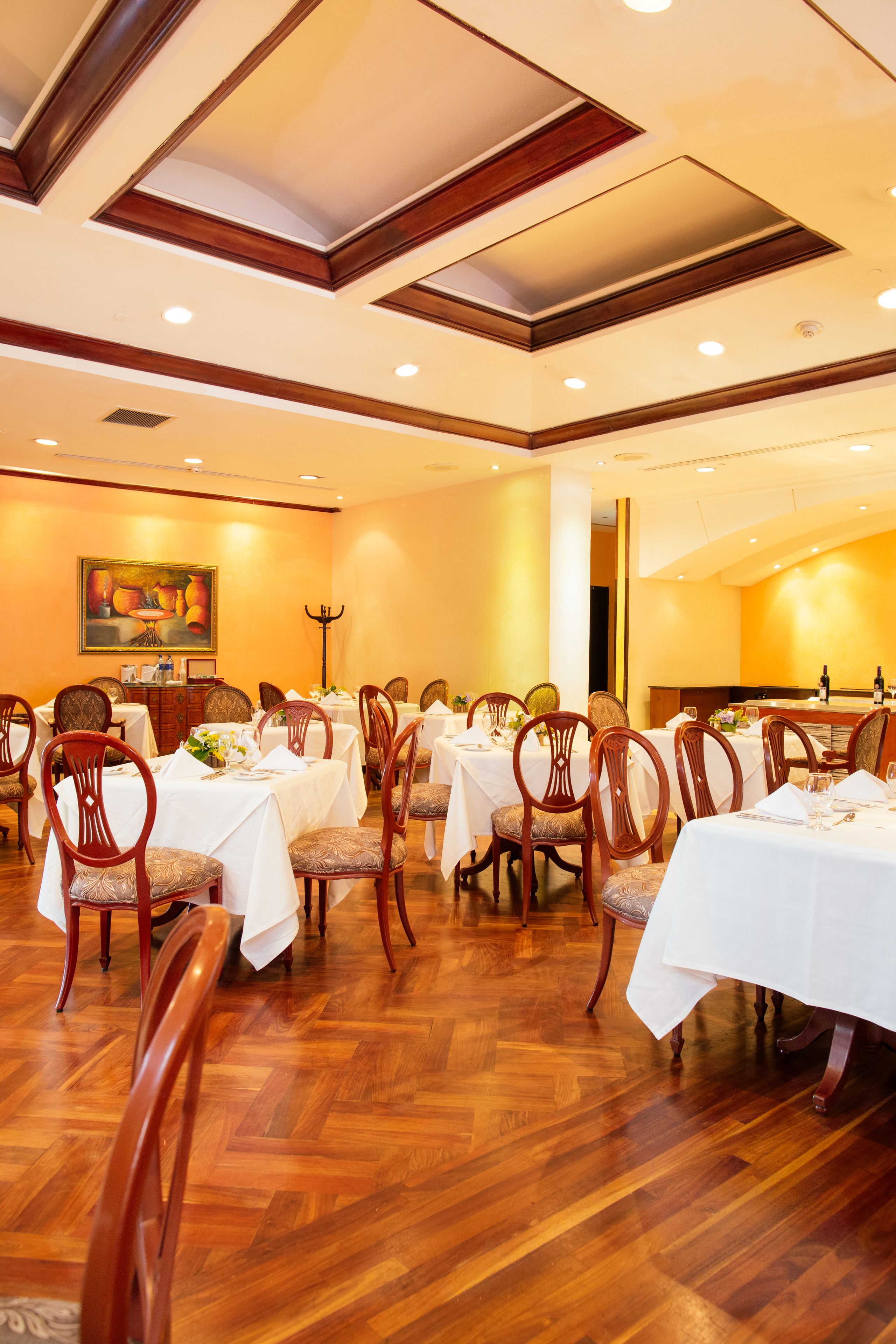 A dining area with multiple tables and chairs, wooden flooring, and a ceiling with recessed lighting.