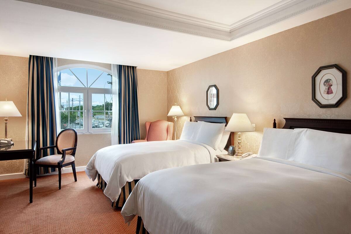A hotel room with two beds, a desk, a chair, and a window with curtains.