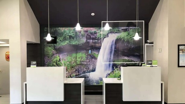 A reception area with a waterfall mural, pendant lighting, and a reception desk. - La Quinta Inn & Suites by Wyndham Minneapolis Northwest (Brooklyn Park)