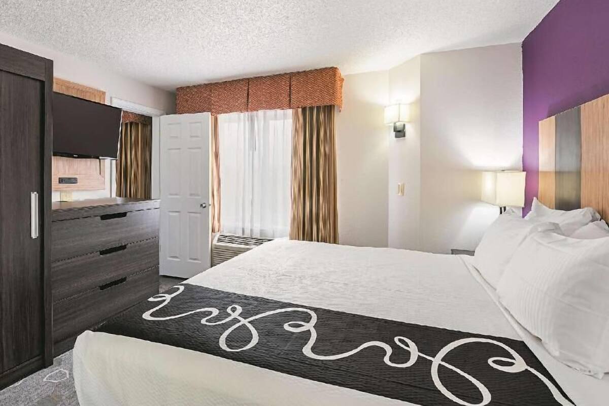 Une chambre d’hôtel avec un lit, une commode, une porte et une fenêtre avec des rideaux.