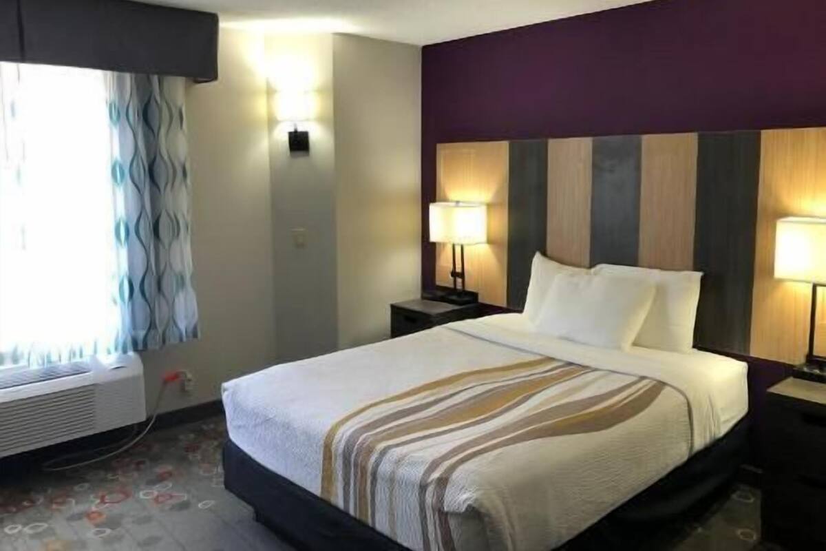 Une chambre d’hôtel comprenant un lit, deux lampes de chevet, une fenêtre avec des rideaux et un climatiseur fixé au mur.