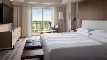 A hotel room with a large bed, a TV, a desk, a chair, and a balcony with a view.