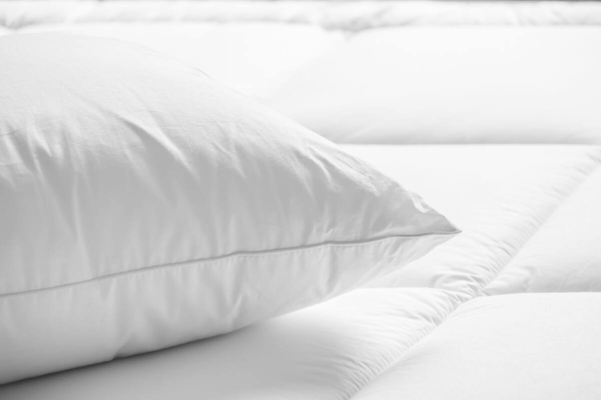 A close-up of a white bed with a neatly arranged pillow and a smooth, unadorned headboard.