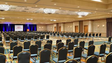 A large conference room with rows of chairs, a stage with a screen, and chandeliers.
