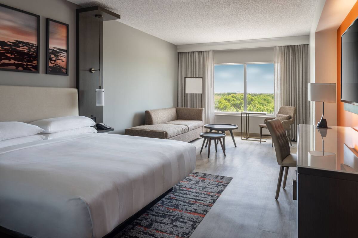 A hotel room with a large bed, a sofa, a desk, and a view of the outdoors.