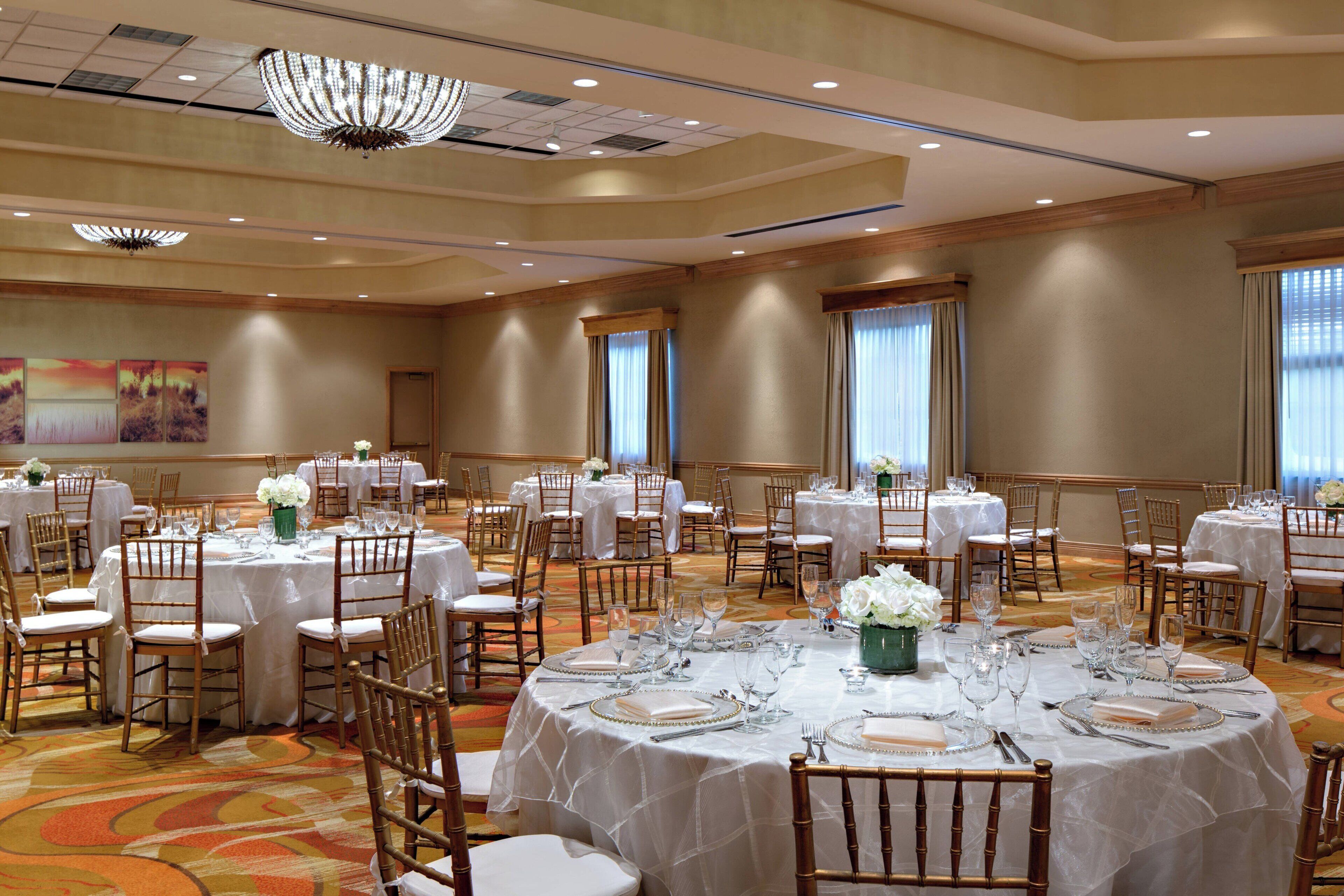 Un salón de banquetes con mesas redondas dispuestas para el servicio de comidas, con manteles blancos y platos con detalles dorados.