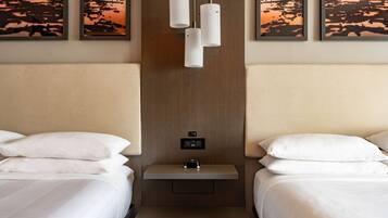 A hotel room with two beds, a small table, and pendant lights.