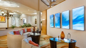 Un lobby moderno de hotel con una zona de estar curva, una mesa de centro de vidrio y una pared grande con tres pinturas abstractas.