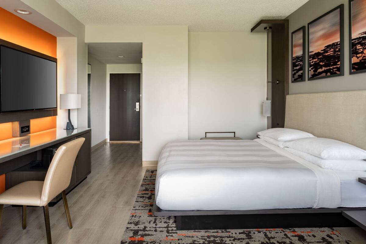A modern hotel room with a bed, a desk, and a TV.