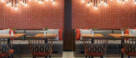 A modern restaurant with a geometric patterned wall, wooden tables and chairs, and hanging light fixtures.