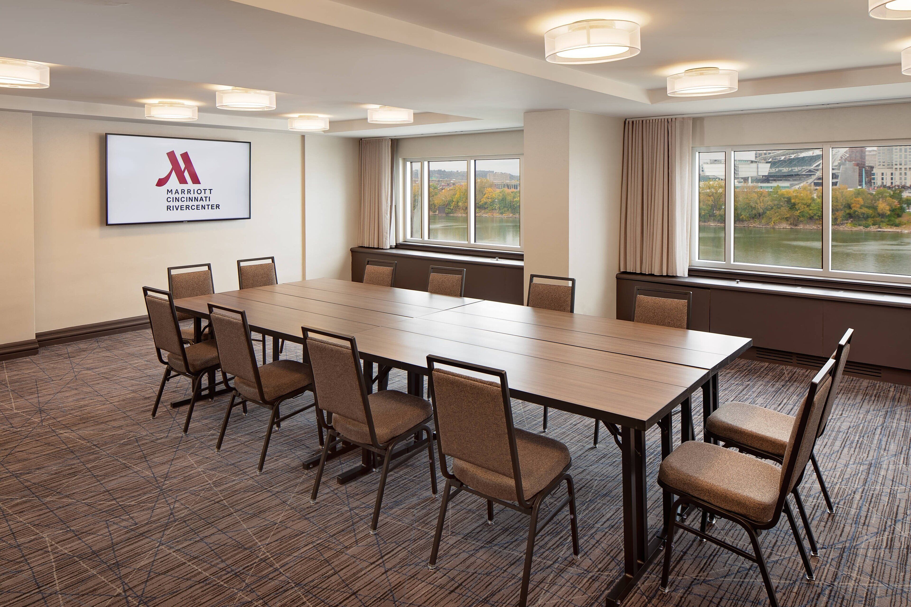 A conference room with a long table, six chairs, and a large window with a view of a river and buildings.
