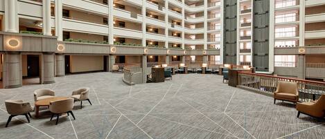 Un vestíbulo de hotel de varios niveles con un piso de diseño geométrico, varias zonas de estar y un mostrador de recepción central.