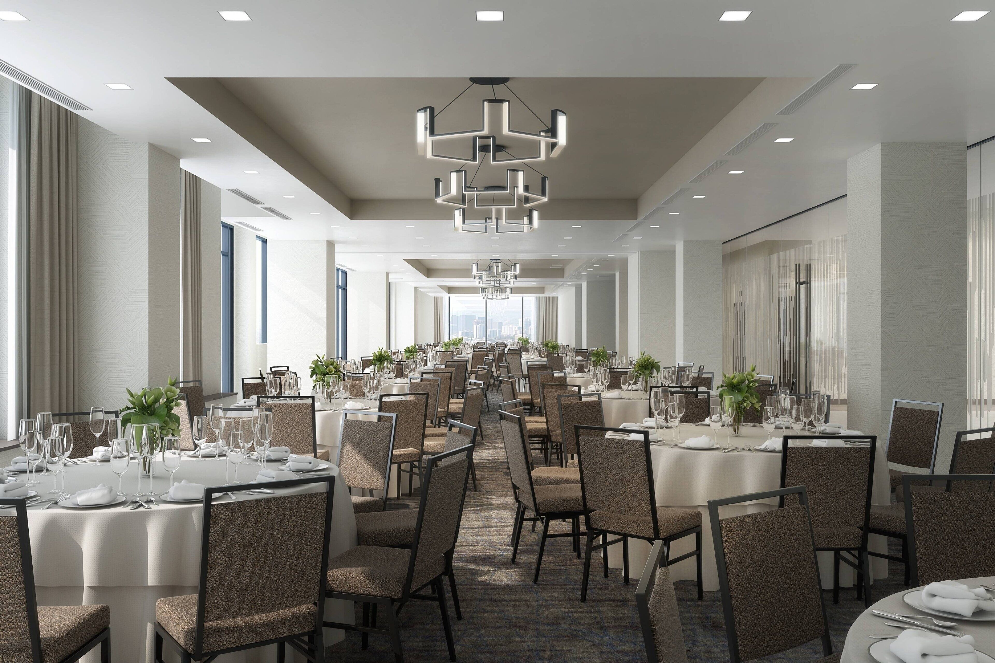 A spacious hotel dining area with multiple round tables, chairs, and modern chandeliers.