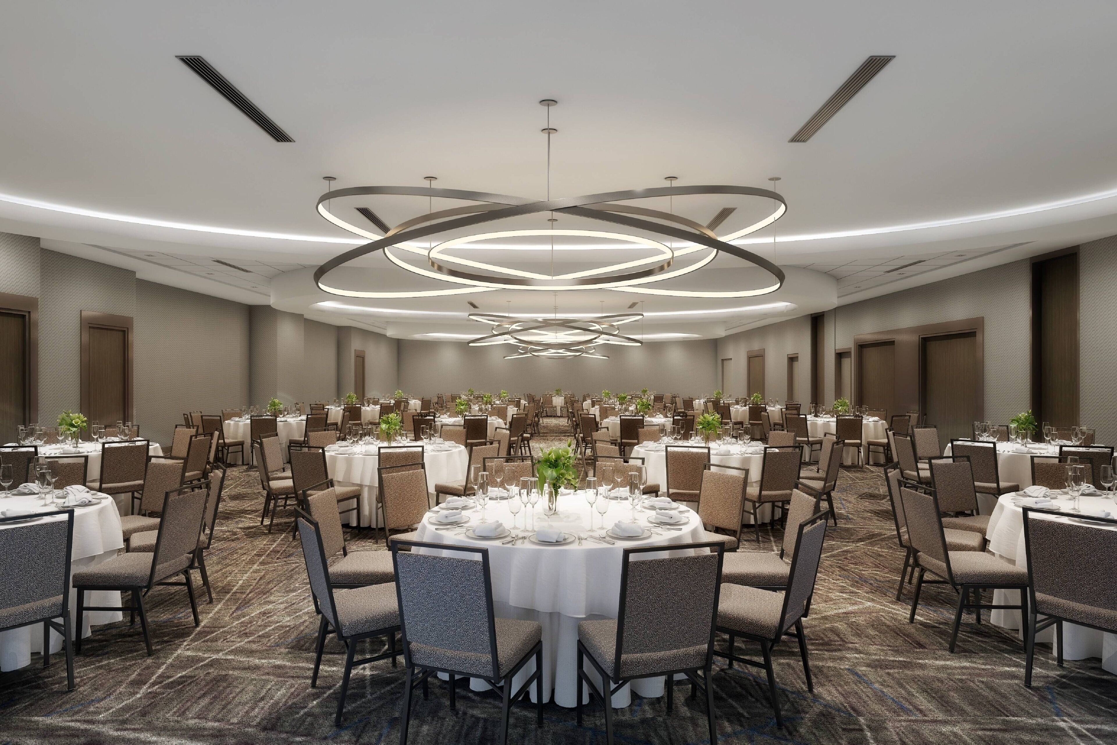 A large banquet hall with round tables, chairs, and a modern chandelier.