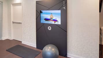 A hallway with a yoga mat, a stationary exercise ball, and a TV screen displaying a yoga pose.