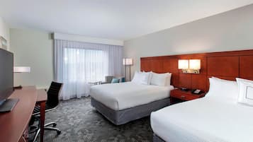 A hotel room with two beds, a desk, a chair, a TV, and a window with curtains.