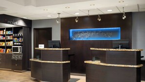 A hotel reception area with a dark wood reception desk, a digital display, and a snack vending machine. - Courtyard by Marriott Myrtle Beach Barefoot Landing (Myrtle Beach)
