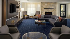 A modern living room with a sectional sofa, armchairs, a glass coffee table, a flat-screen TV, and a stone accent wall. - Courtyard by Marriott Myrtle Beach Barefoot Landing (Myrtle Beach)