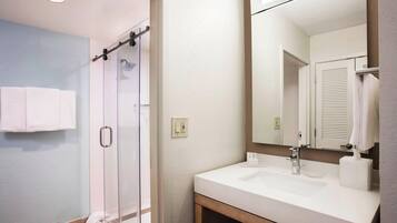 A bathroom with a glass shower, a sink, and a mirror.