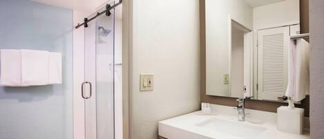 A bathroom with a glass shower, a sink, and a mirror.