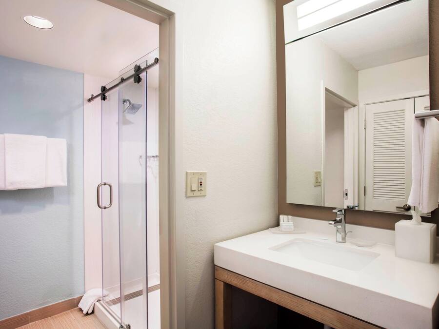 A bathroom with a glass shower, a sink, and a mirror.