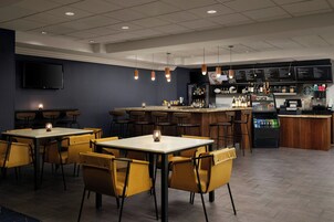 A restaurant with tables and chairs, a bar area with a menu board, and a television mounted on the wall.