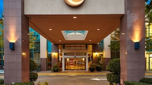 A modern hotel entrance with a prominent logo, a glass facade, and a well-lit entrance area.