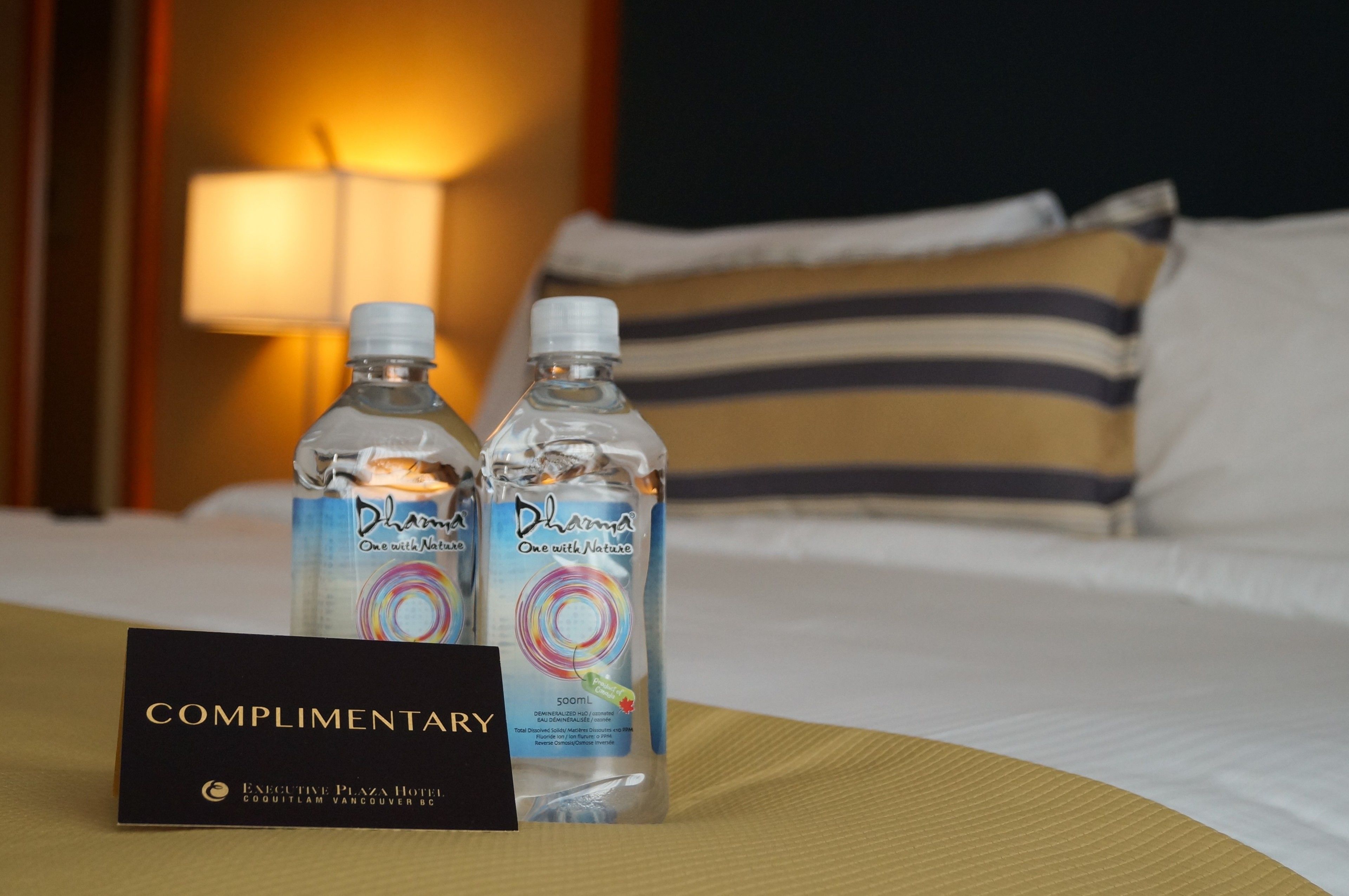 Deux bouteilles d’eau Dharma sur un lit d’hôtel, accompagnées d’une pancarte indiquant qu’elles sont offertes gratuitement.