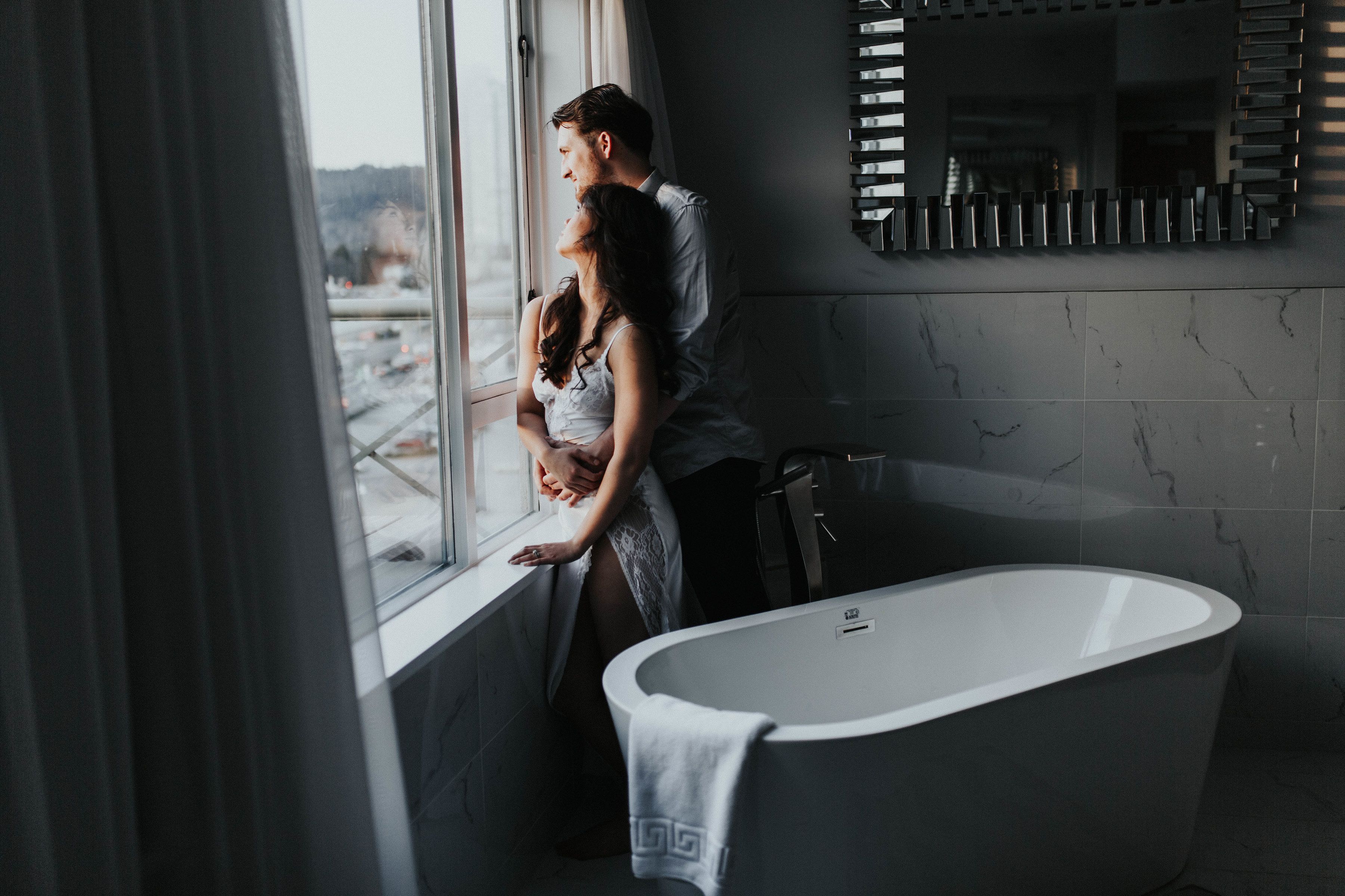 Un baño moderno con una bañera independiente, un ventanal grande y un espejo con persianas horizontales.
