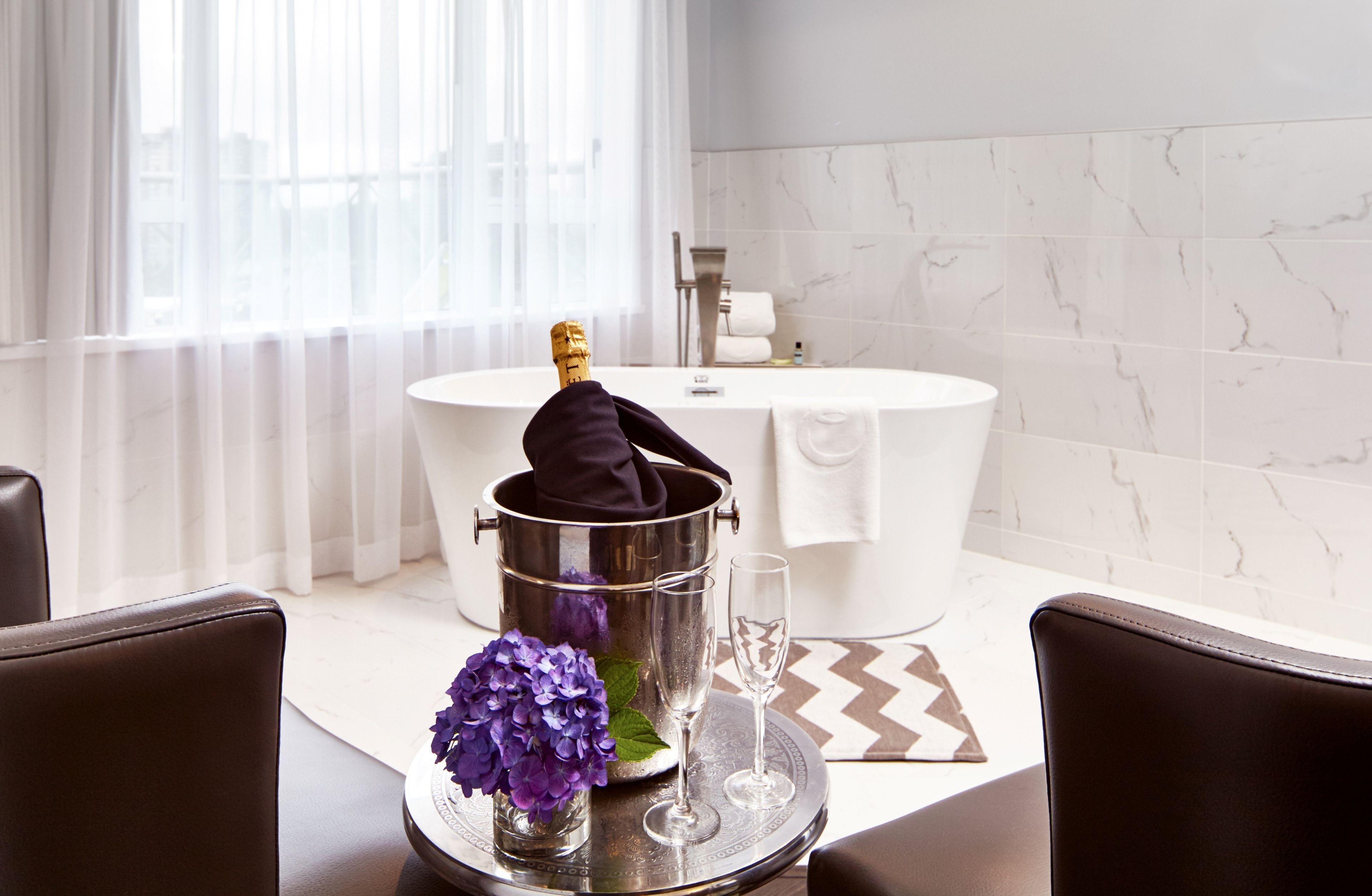 A modern bathroom with a bathtub, a champagne bottle, and a glass on a tray.