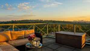 A balcony with a sofa, a table with cups and flowers, and a view of a city skyline.