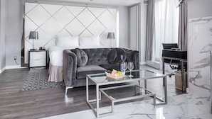 Una habitación de hotel moderna con una cama grande, un sofá gris, una mesa de centro de vidrio y un piano.