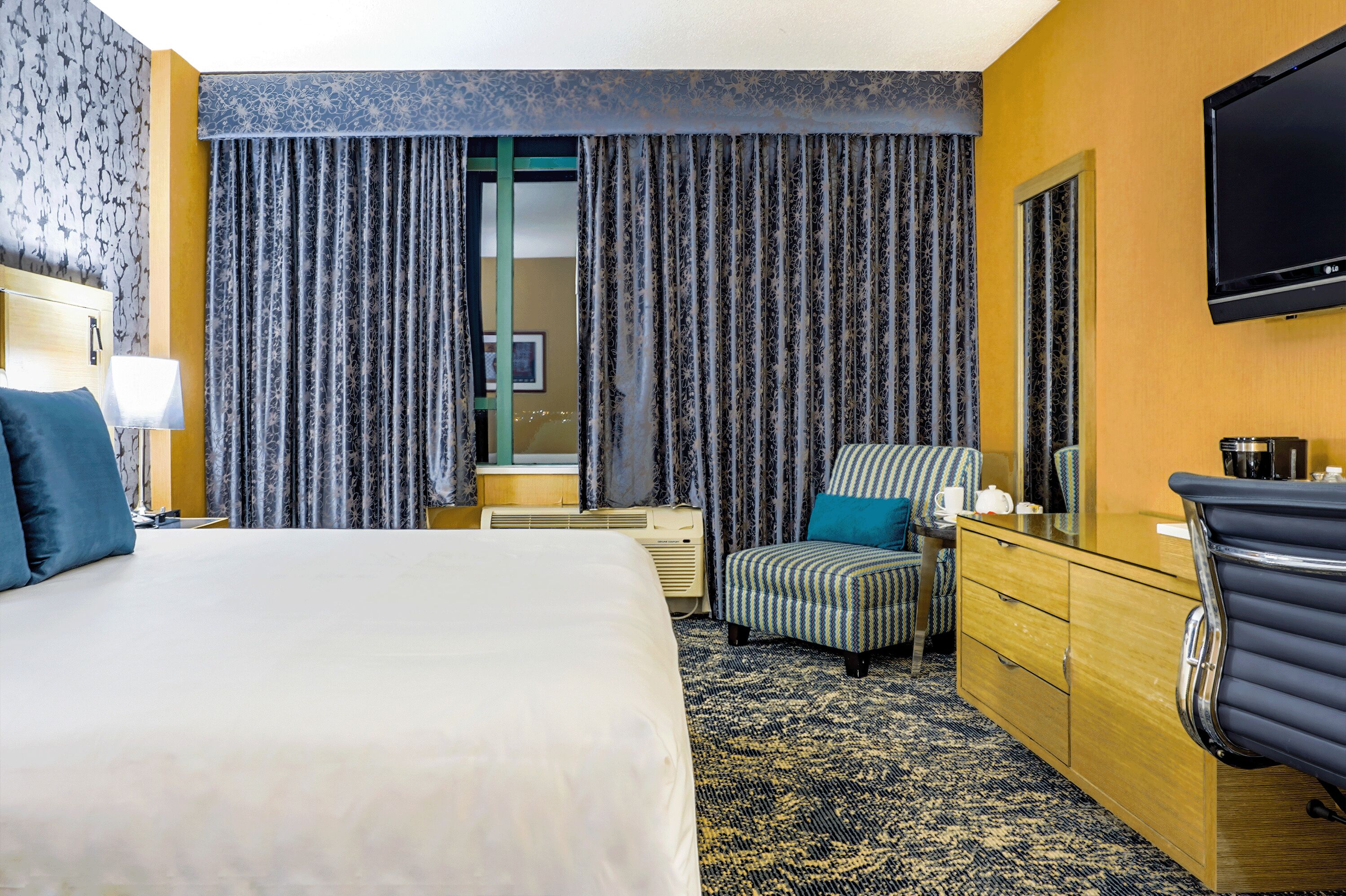 A hotel room with a large bed, a desk with a flat-screen TV, a chair, and a dresser.