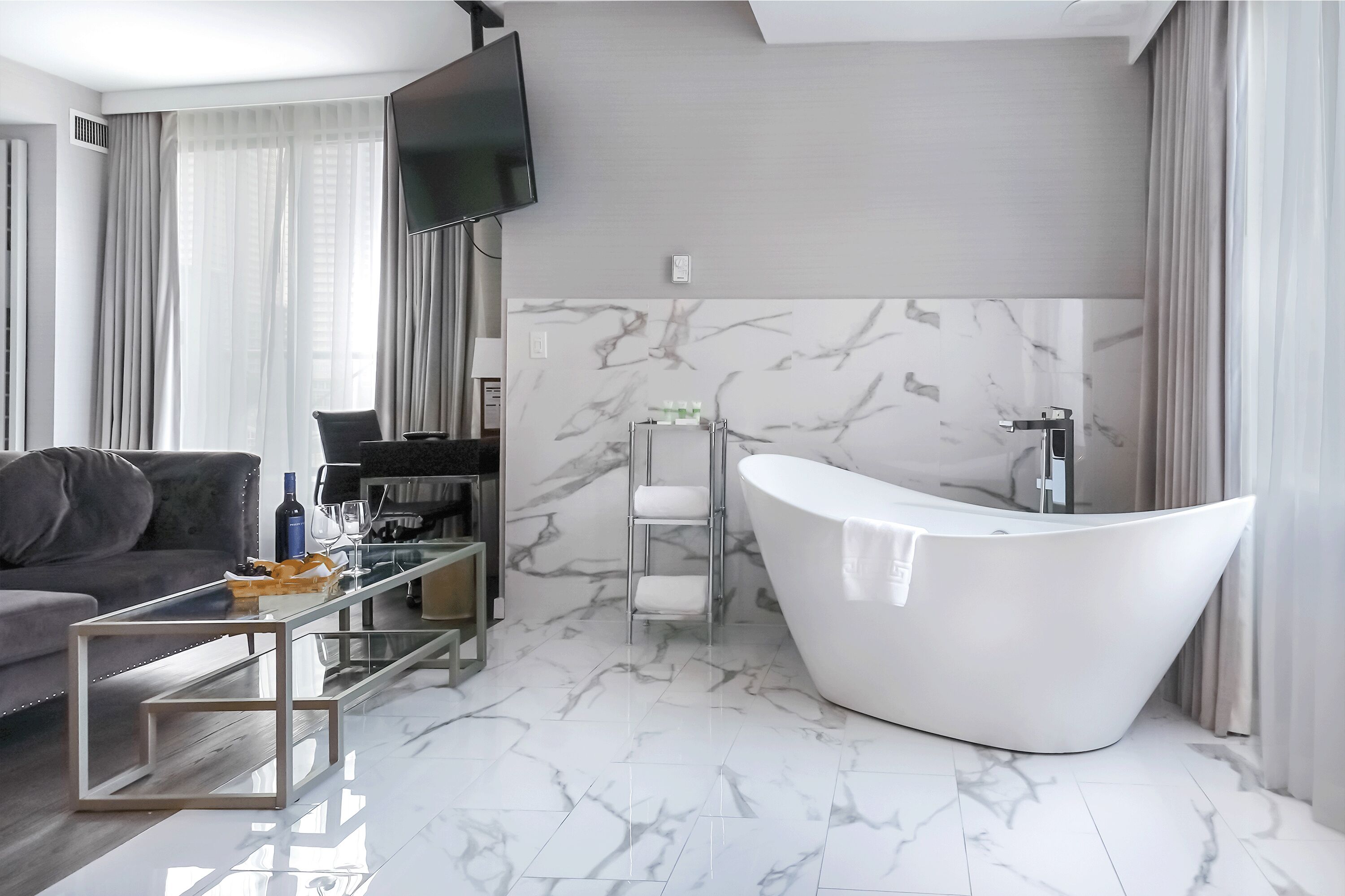 Een moderne badkamer met een vrijstaand bad, een glazen bijzettafeltje en een bank in een woonruimte.