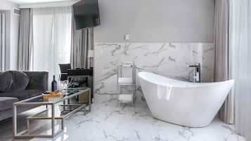 Een moderne badkamer met een vrijstaand bad, een glazen bijzettafeltje en een bank in een woonruimte.