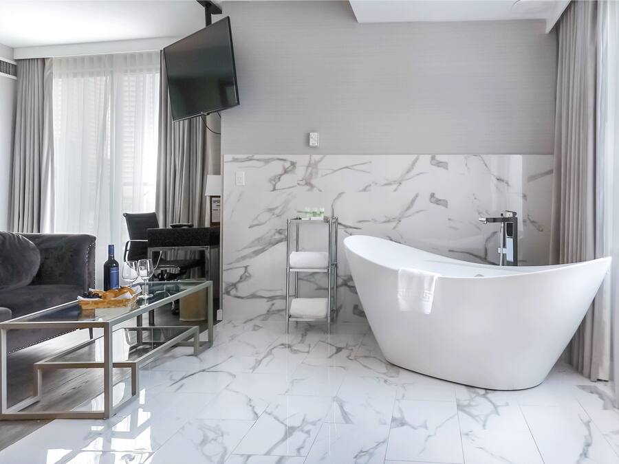 Een moderne badkamer met een vrijstaand bad, een glazen bijzettafeltje en een bank in een woonruimte.
