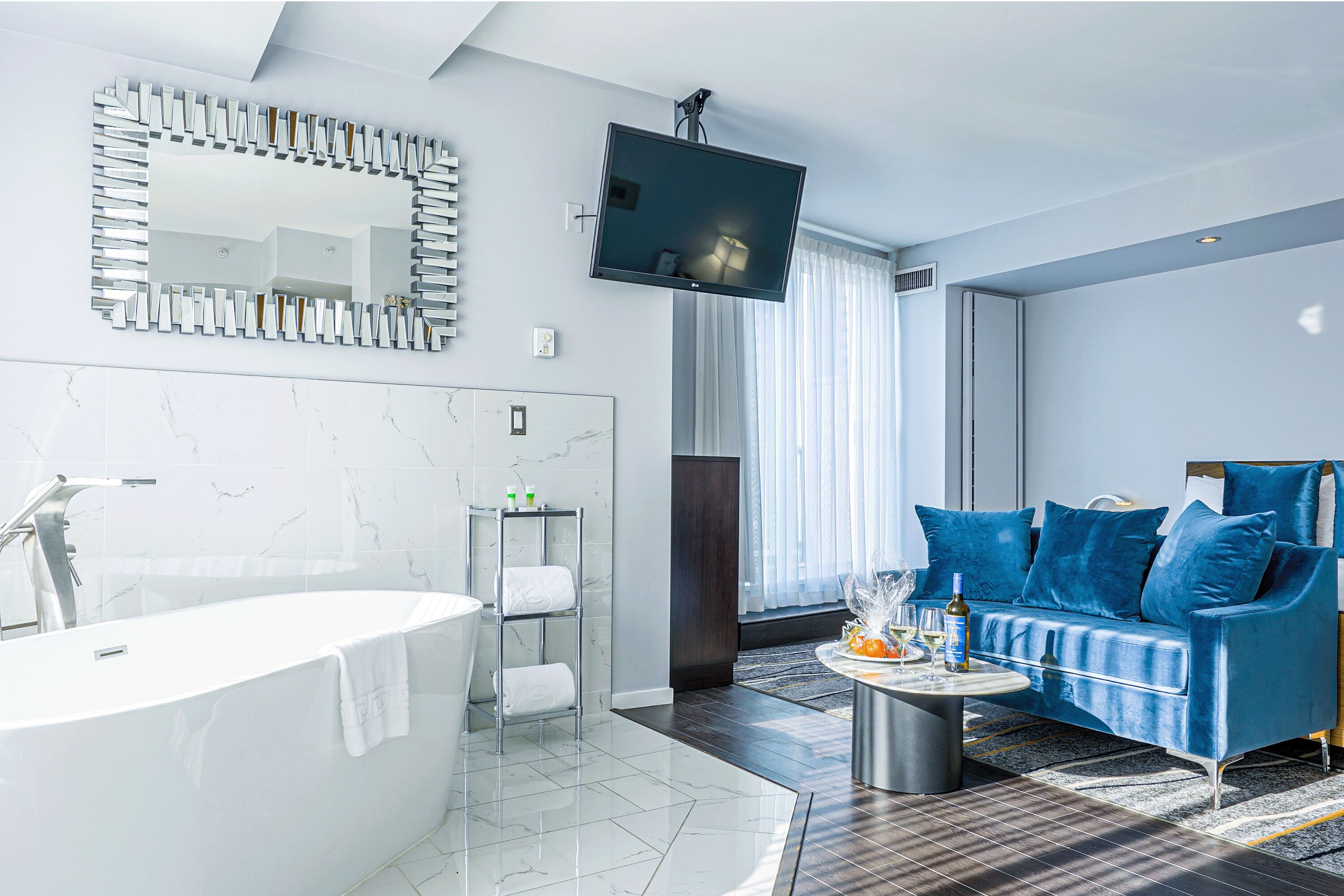 A modern bathroom with a bathtub, a vanity, a mirror, and a television mounted above the tub.