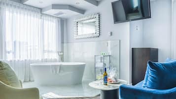 Un baño moderno con una bañera independiente, un espejo grande, un televisor de pantalla plana y una zona de estar con un sillón azul.