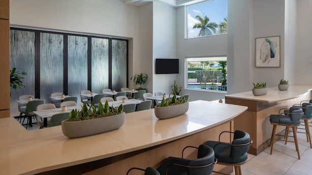 Un moderno hall de hotel con un amplio mostrador de recepción, varias zonas de estar y grandes ventanales que ofrecen vistas a palmeras.