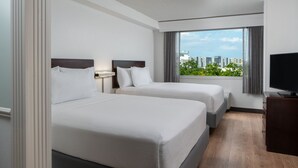 Habitación de hotel con dos camas, televisión y vistas a edificios a través del ventanal.