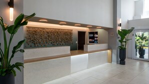 Una zona de recepción con mostrador de mármol, luminarias fijadas a la pared y plantas en macetas.