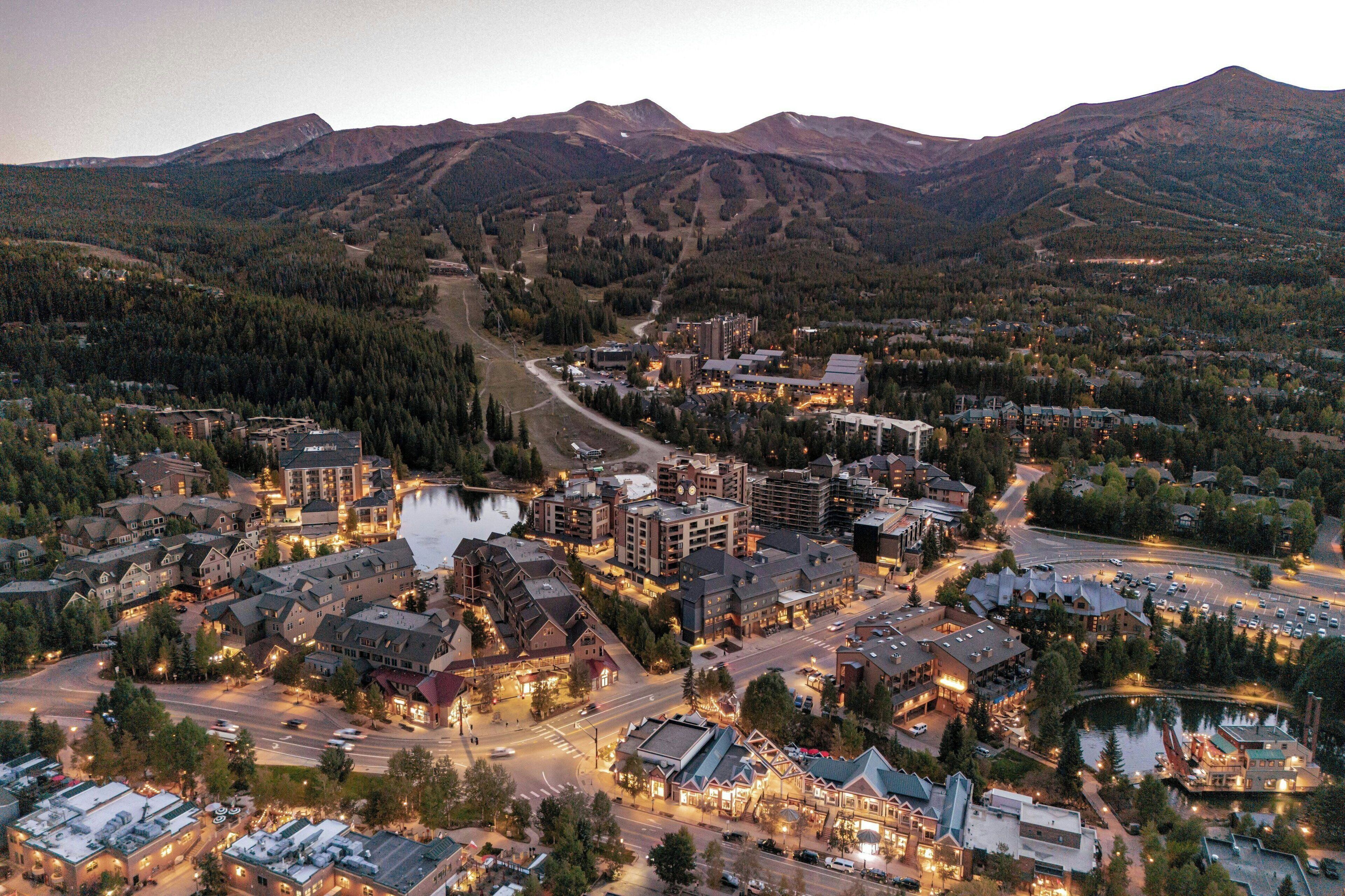 An aerial view of a town with a mix of residential and commercial buildings, a central road, and a body of water.