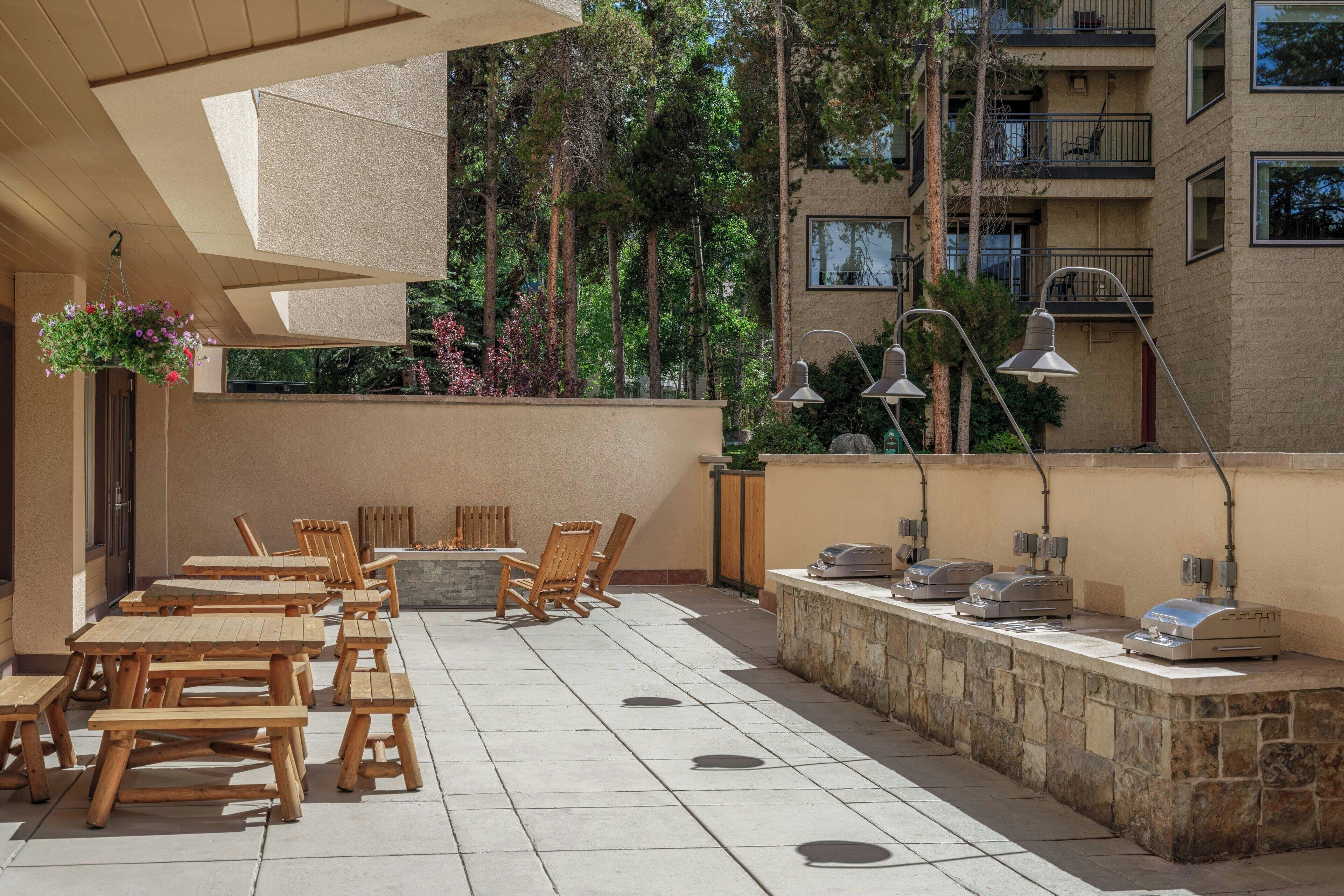 An outdoor patio with wooden tables and chairs, a stone wall, and outdoor lighting.